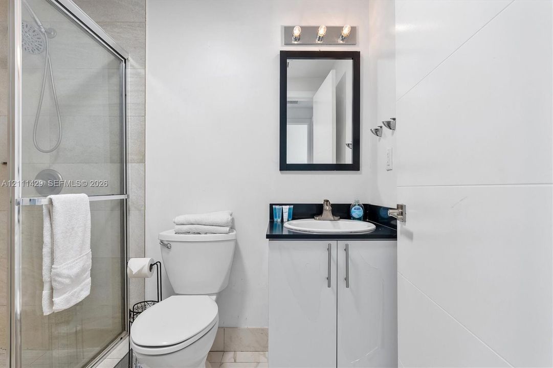 Bathroom featuring a shower with sliding glass doors, a vanity with a dark countertop and white cabinetry, an integrated sink, and a rectangular mirror with a three-light fixture