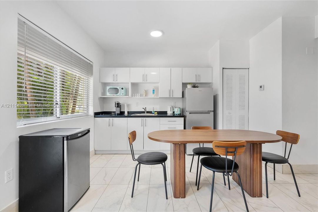 Kitchenette featuring white slab-panel cabinetry, black solid-surface countertops, recessed lighting, and white stone-finish tile flooring