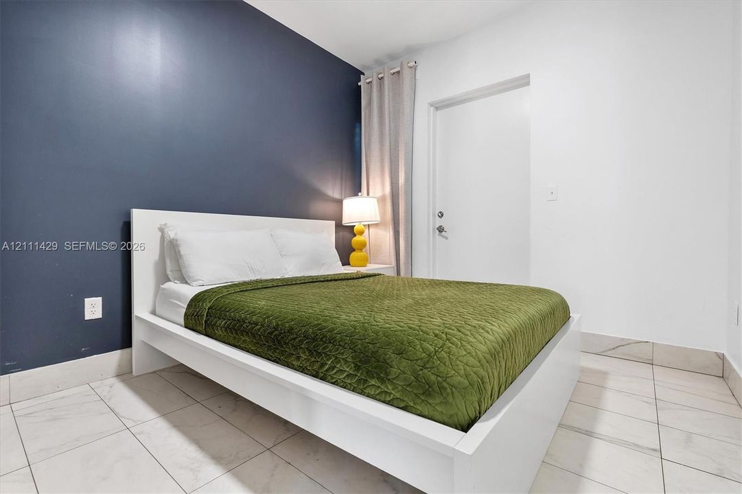 Room featuring light-toned large-format tile flooring, a prominent dark-toned accent wall, and a classic door with a metallic handle