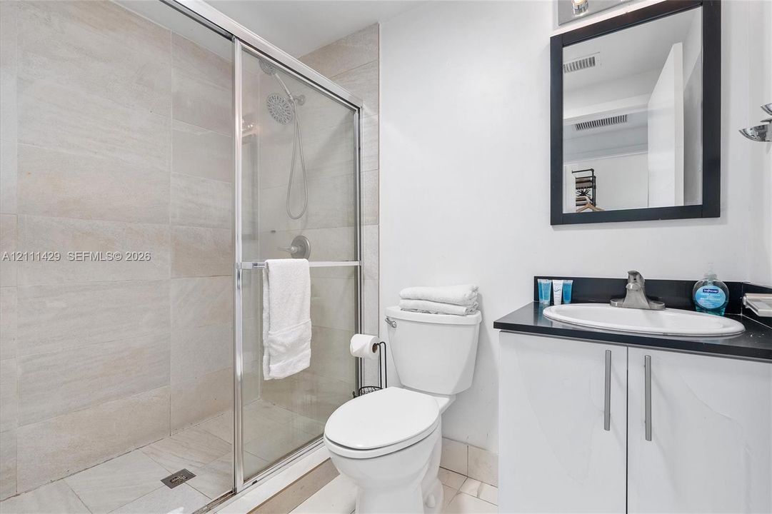 Bathroom featuring a walk-in shower with glass enclosure and large-format tile surround, vanity with dark countertop, integrated sink, and wall-mounted mirror with black frame