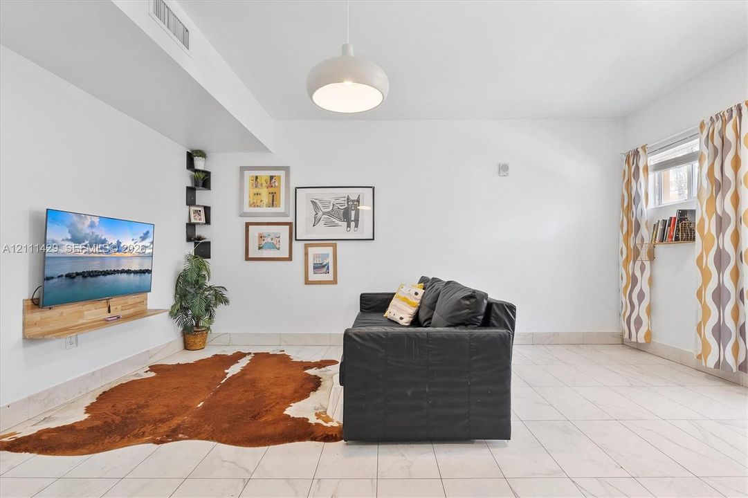 Neutral tile flooring, custom floating wood-finish media console, built-in corner display shelving, and modern dome pendant lighting