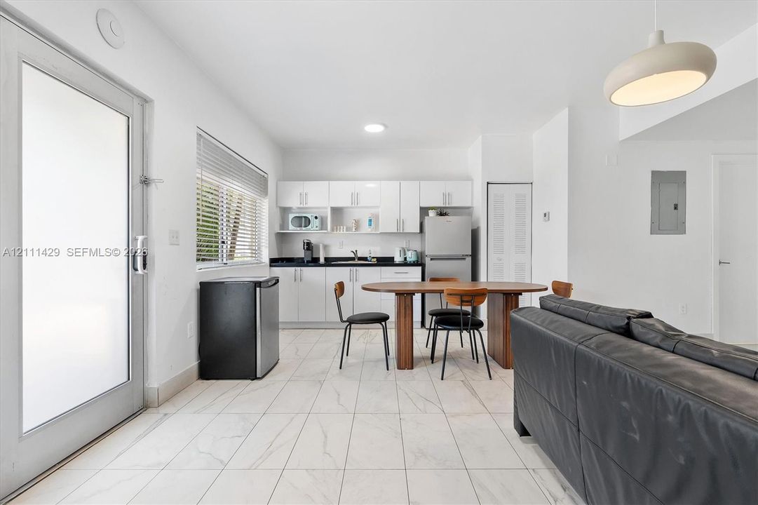 Open living and dining area with a wood dining table, black chairs, white kitchenette cabinetry, a stainless steel refrigerator and a louvered closet door