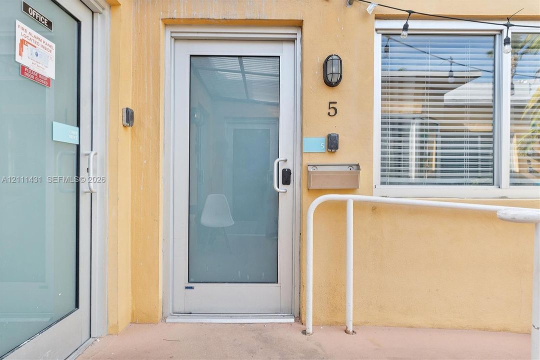 Full-glass entry door with metallic frame, wall-mounted exterior sconce, brushed metal mailbox, and aluminum handrail