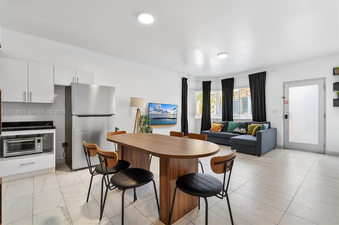 Open-concept kitchen area featuring white cabinetry, stainless steel refrigerator, stone-style countertops, light-toned tiled flooring, and a large bay window