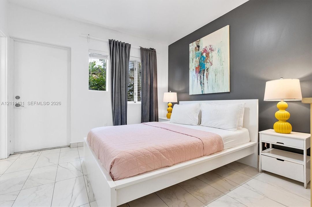 Bedroom featuring large-format tile flooring, a charcoal accent wall, and a window with horizontal blinds