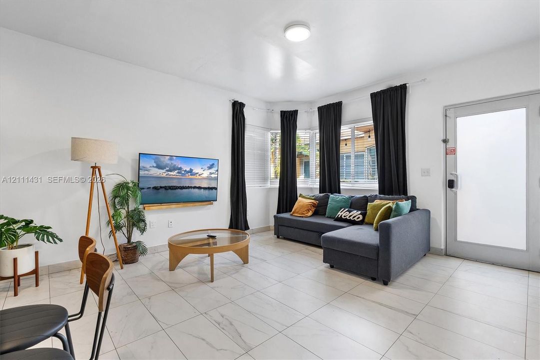 Living space featuring large-format tile flooring, a recessed bay window, flush-mount ceiling lighting, and a glass-paneled exterior door