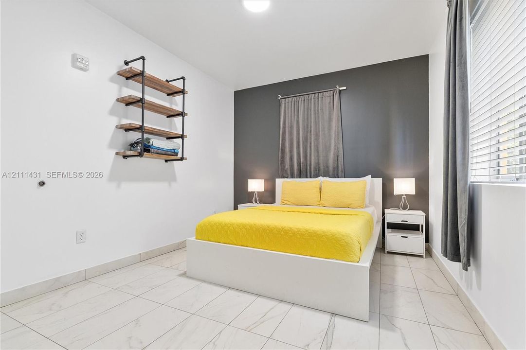 Room featuring large-format tile flooring, a dark charcoal accent wall, and wall-mounted industrial-style shelving with wood-finish surfaces and black pipe supports