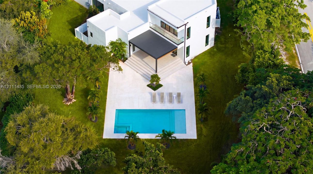 Contemporary residence featuring a white stucco exterior, covered patio, rectangular swimming pool, stone-paver pool deck, and mature landscaping