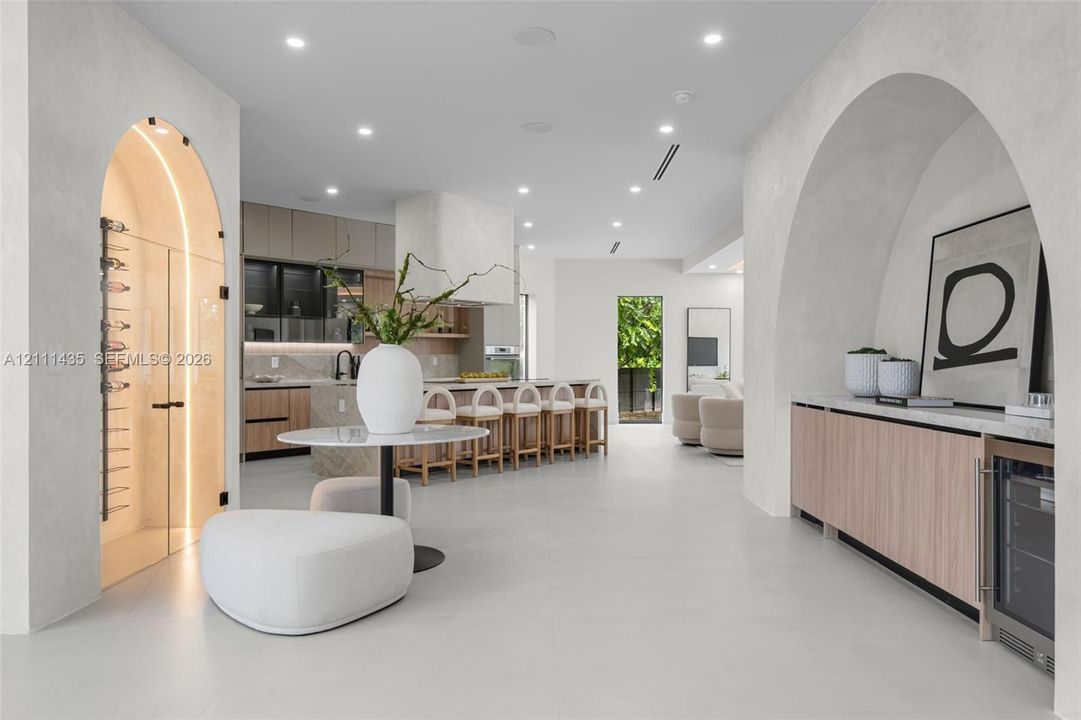 Open-concept floor plan featuring arched architectural entryways, a climate-controlled glass wine cellar, custom light wood cabinetry, and recessed lighting