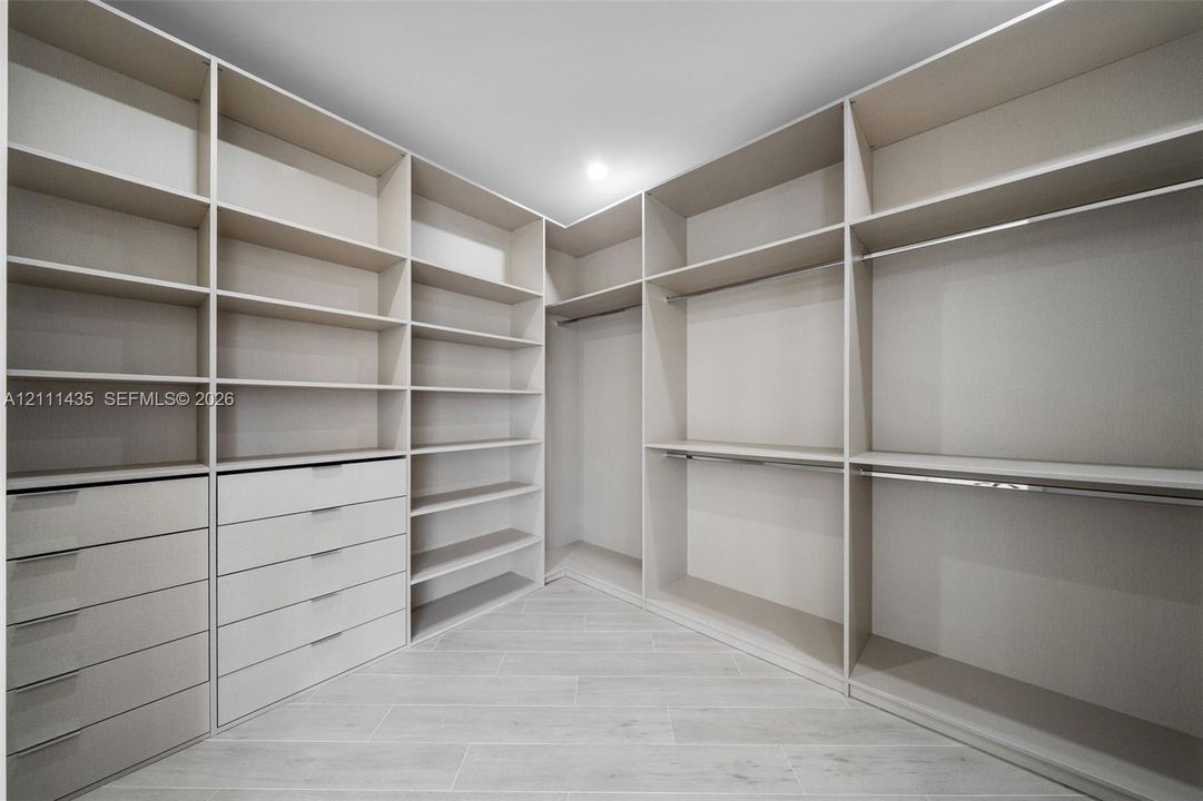 Walk-in closet featuring extensive built-in shelving, integrated multi-drawer cabinetry, dual-level hanging rods, and light-toned tile flooring