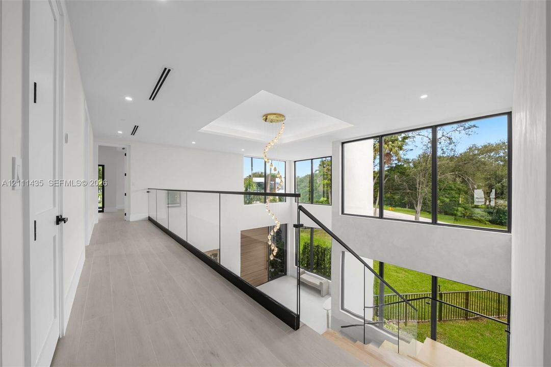Open landing featuring wood-finish flooring, glass panel railing with metal accents, recessed lighting, and expansive floor-to-ceiling windows