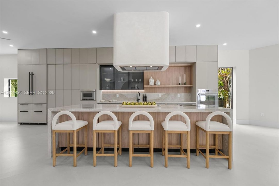 Kitchen featuring a waterfall-edge island, custom cabinetry, integrated high-end appliances, a stone-finish backsplash, and a floating range hood