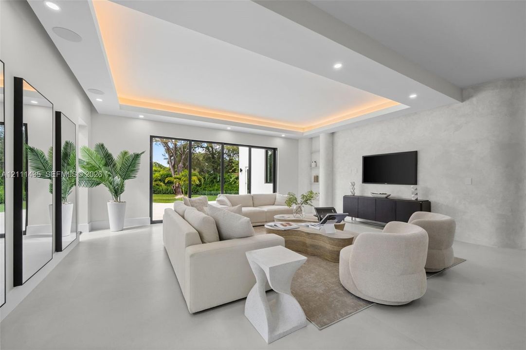 Living area featuring a coffered ceiling with integrated cove lighting, recessed ceiling lights, a textured stone-finish accent wall, and multi-panel floor-to-ceiling glass sliding doors
