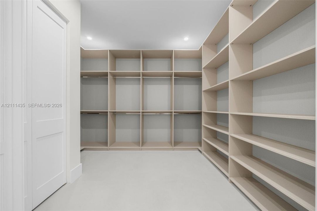 Custom walk-in storage area featuring extensive built-in shelving, integrated hanging rods, crisp white walls, and recessed lighting