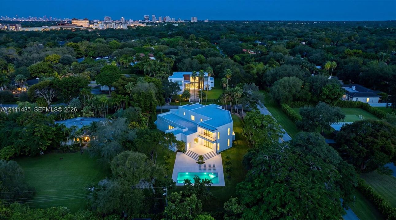 Aerial perspective featuring a multi-level contemporary residence, expansive manicured grounds, a rectangular swimming pool, and mature foliage