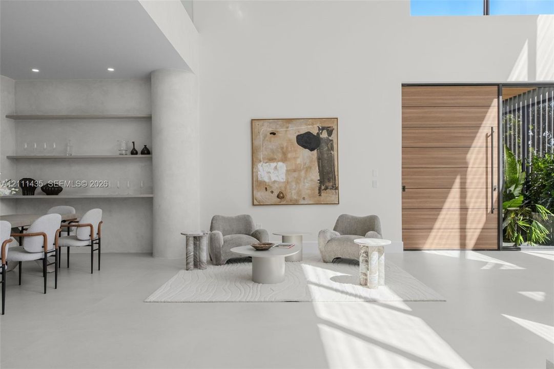 Double-height ceiling with recessed lighting, integrated stone shelving, polished concrete flooring, oversized wood-finish front entry door, and floor-to-ceiling glass wall