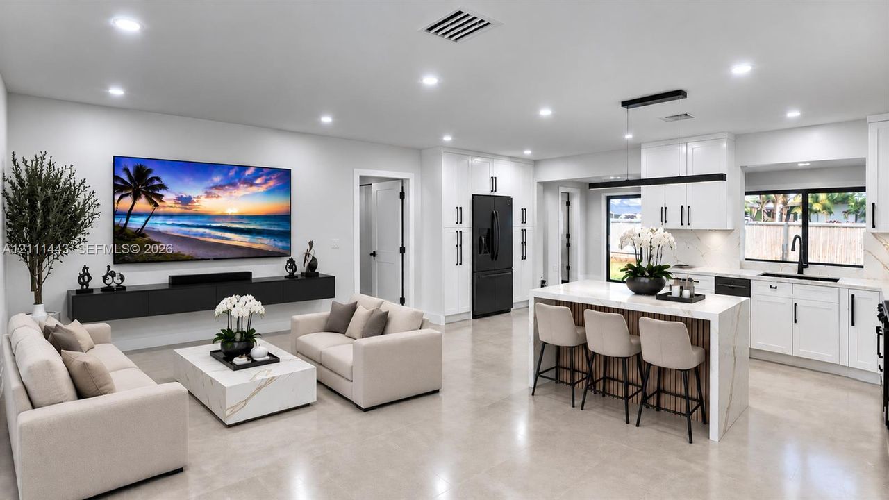 Open-concept living space featuring high-gloss white cabinetry, a large kitchen island with stone-finish countertops, floating wall-mounted storage, recessed lighting, and large-format tile flooring