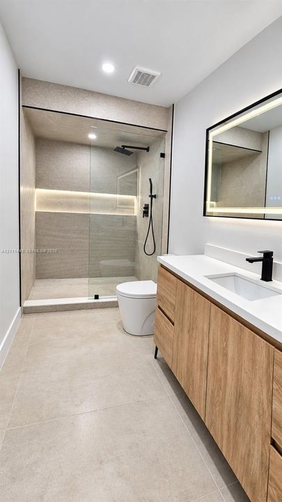 Walk-in shower with integrated wall lighting and matte black rainfall fixture, wood-finish floating vanity with quartz countertop, and rectangular LED-backlit mirror