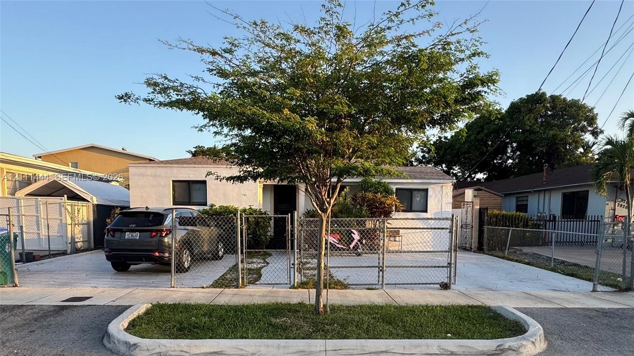 Single-story stucco exterior featuring a concrete driveway, gated entry, and mature landscaping