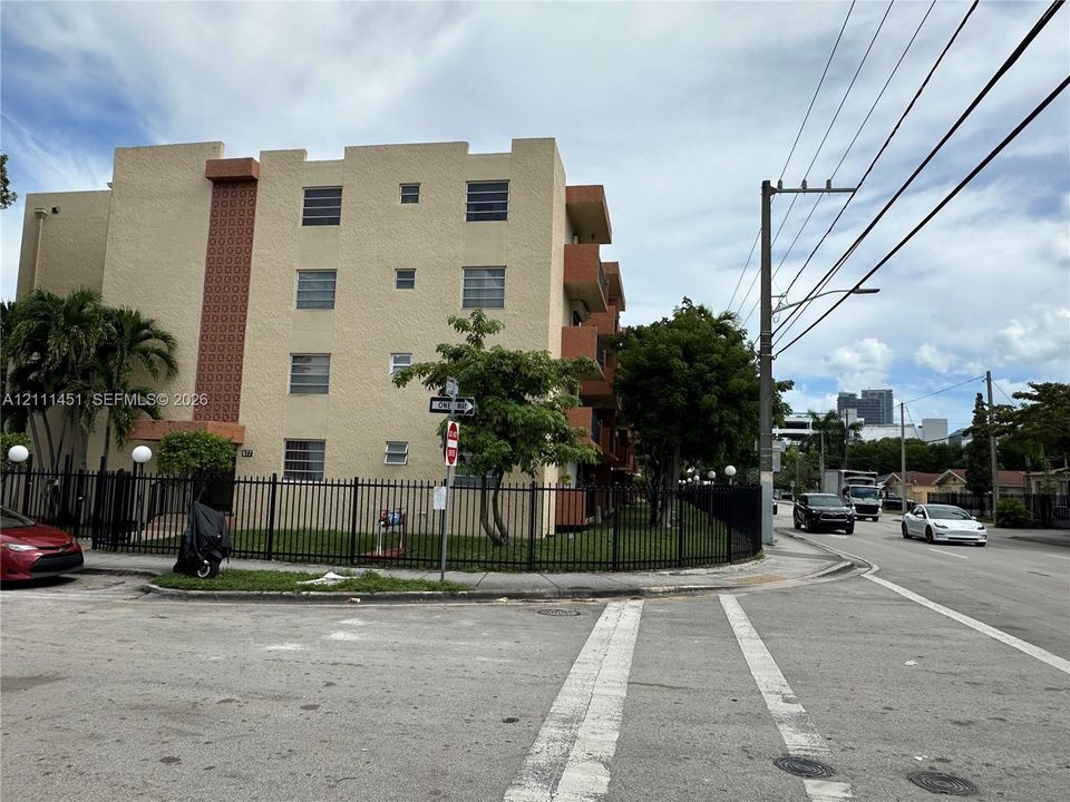 Multi-story exterior featuring a textured stucco facade, decorative geometric masonry accents, fixed-louver windows, and perimeter metal fencing