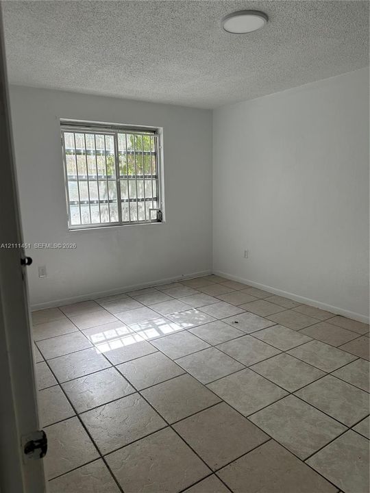 Neutral-toned tile flooring, textured ceiling finish, and a window with security bars