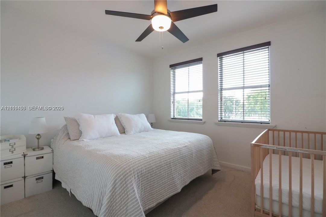 Neutral-toned carpeted bedroom featuring two windows with installed blinds and a centrally mounted ceiling fan