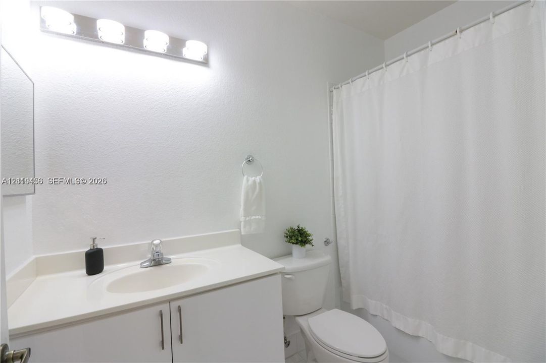 Bathroom featuring a white vanity cabinet, integrated sink, multi-bulb wall-mounted vanity lighting, and a shower-tub combination
