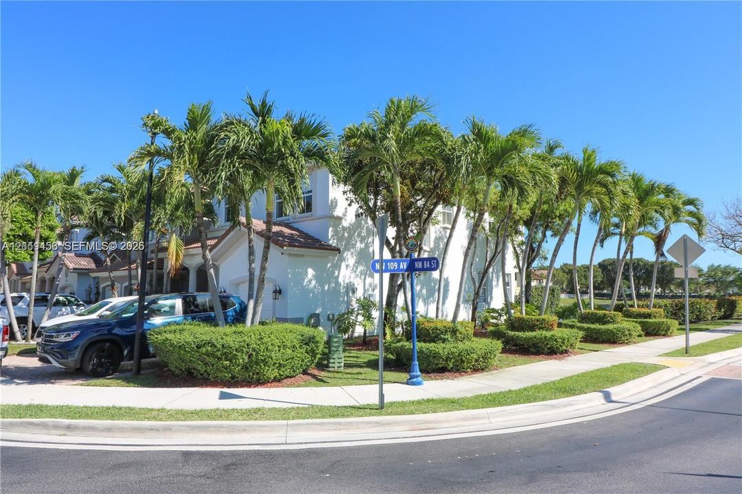 Two-story exterior featuring light-toned stucco siding, a tiled roof, and mature palm tree landscaping