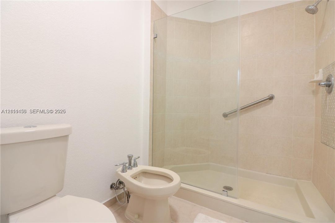 Walk-in shower with a glass enclosure, neutral tile surround, and metal grab bar, accompanied by a bidet and toilet