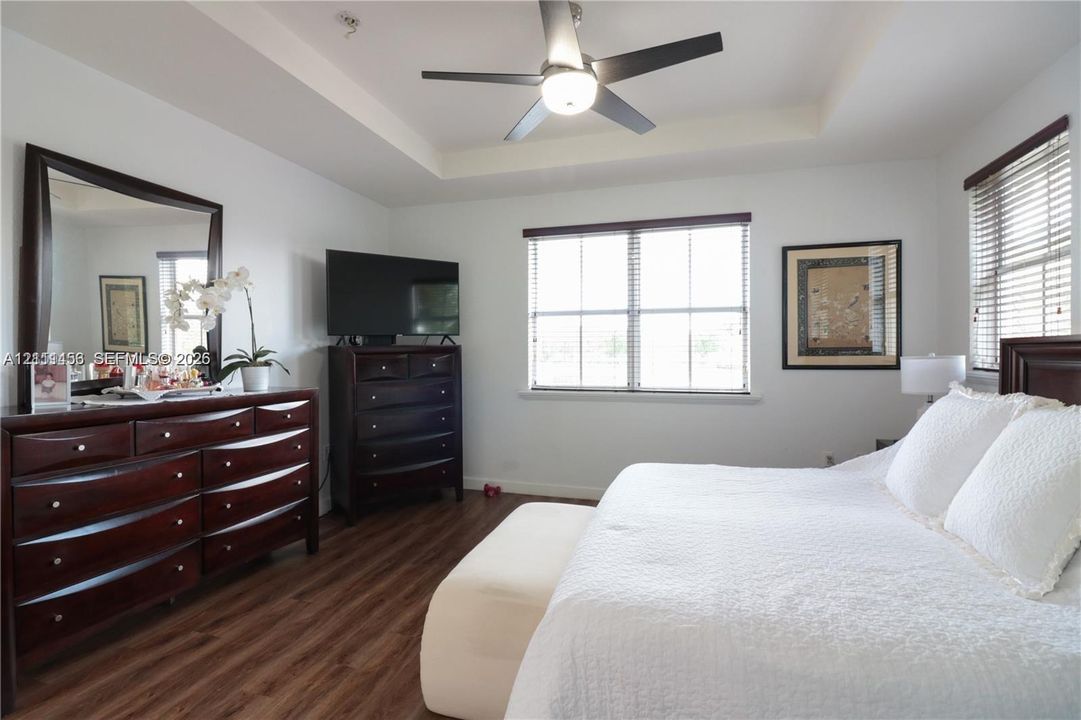 Tray ceiling, wood-finish flooring, ceiling fan with integrated lighting, and horizontal window blinds