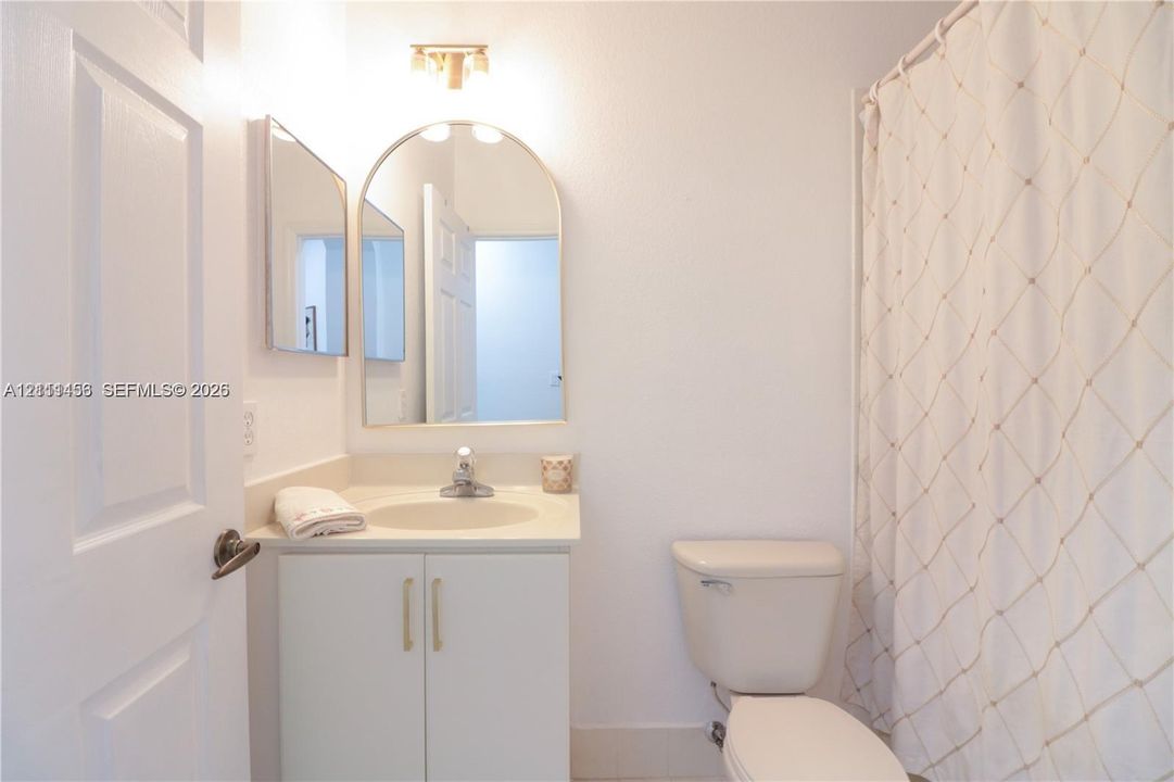 Bathroom featuring a white vanity cabinet, solid-surface countertop with integrated sink, arched wall mirror, and dual-light fixture