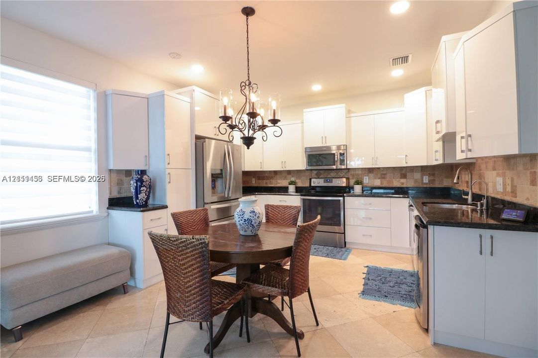Kitchen featuring white cabinetry, dark countertops, tiled backsplash, stainless steel appliances, and tile flooring
