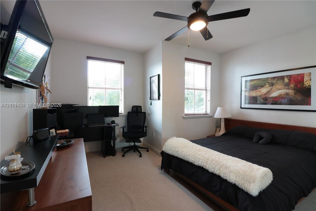 Bedroom featuring neutral carpeting, dual windows with horizontal blinds, and a central ceiling fan with an integrated light fixture