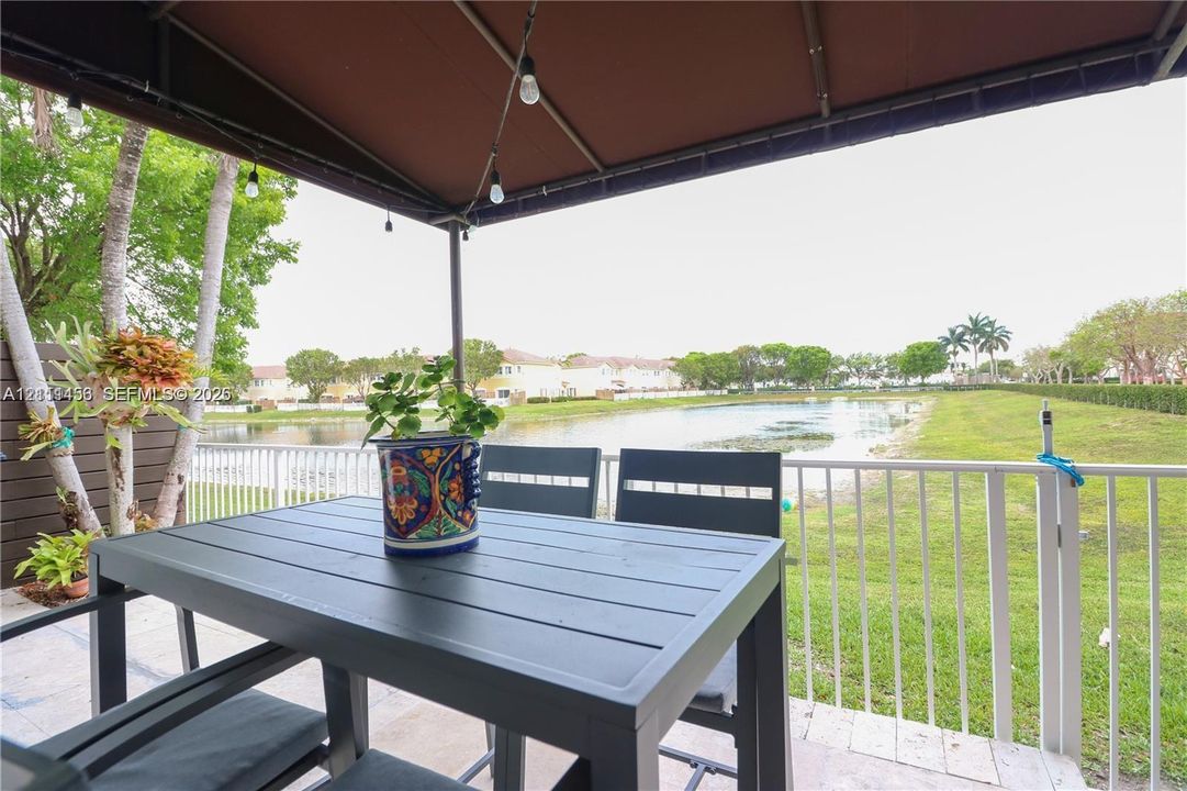 Covered patio featuring a metal awning, paver flooring, and white metal railing, overlooking a pond