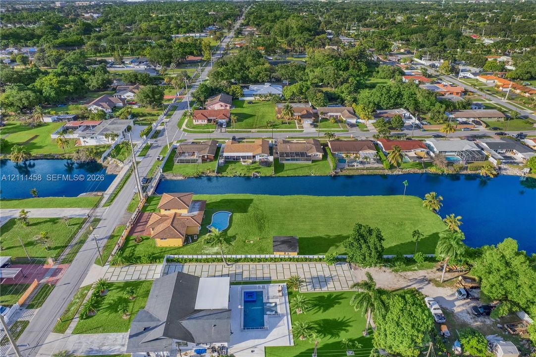 Aerial perspective of a waterfront property featuring a canal-front bulkhead, expansive lawn, swimming pool, and concrete paver driveway