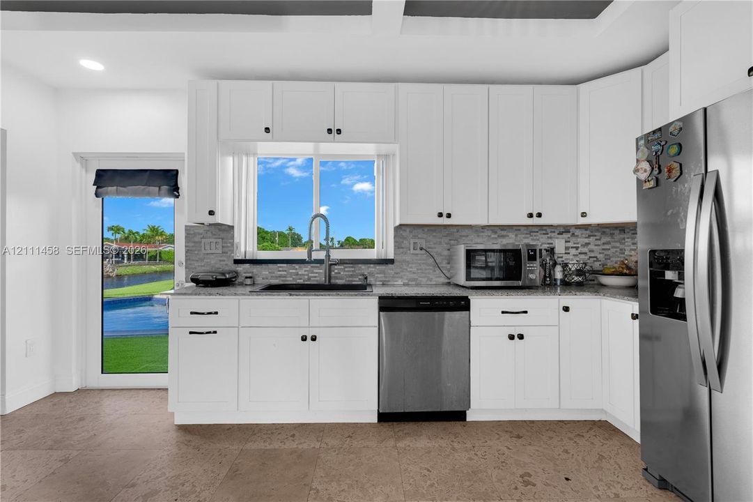 Kitchen featuring white cabinetry, stone-surface countertops, stone-tile backsplash, stainless steel appliances,