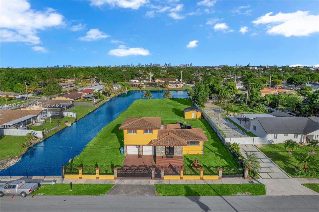 Waterfront residential property featuring expansive lawn space, decorative perimeter fencing, concrete driveway, and attached garage