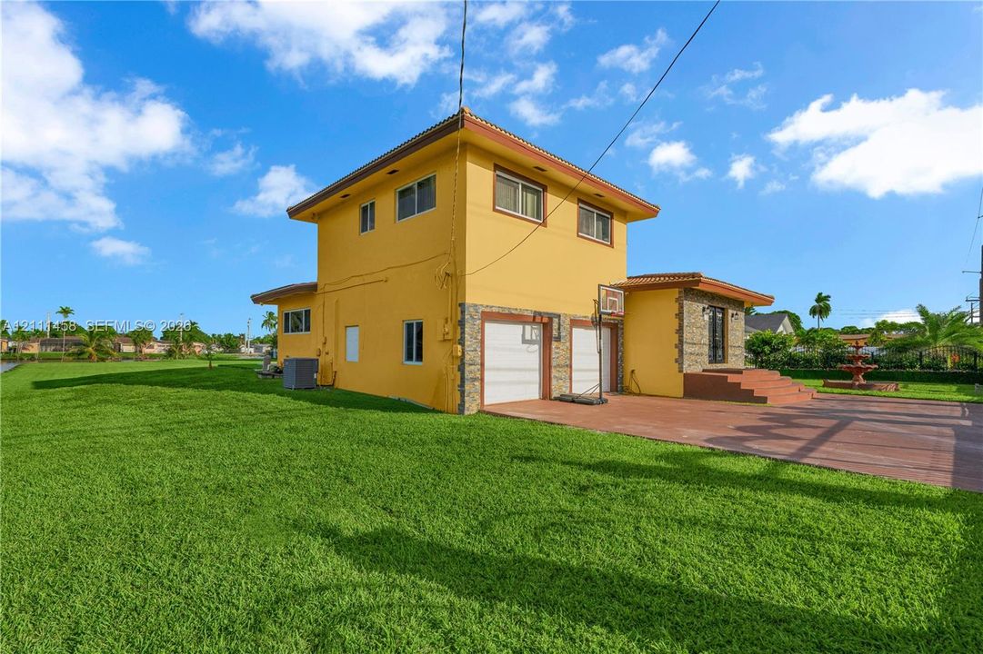 Two-story exterior, stone veneer accents, multi-car garage with white paneled doors, expansive lawn, and paved terrace