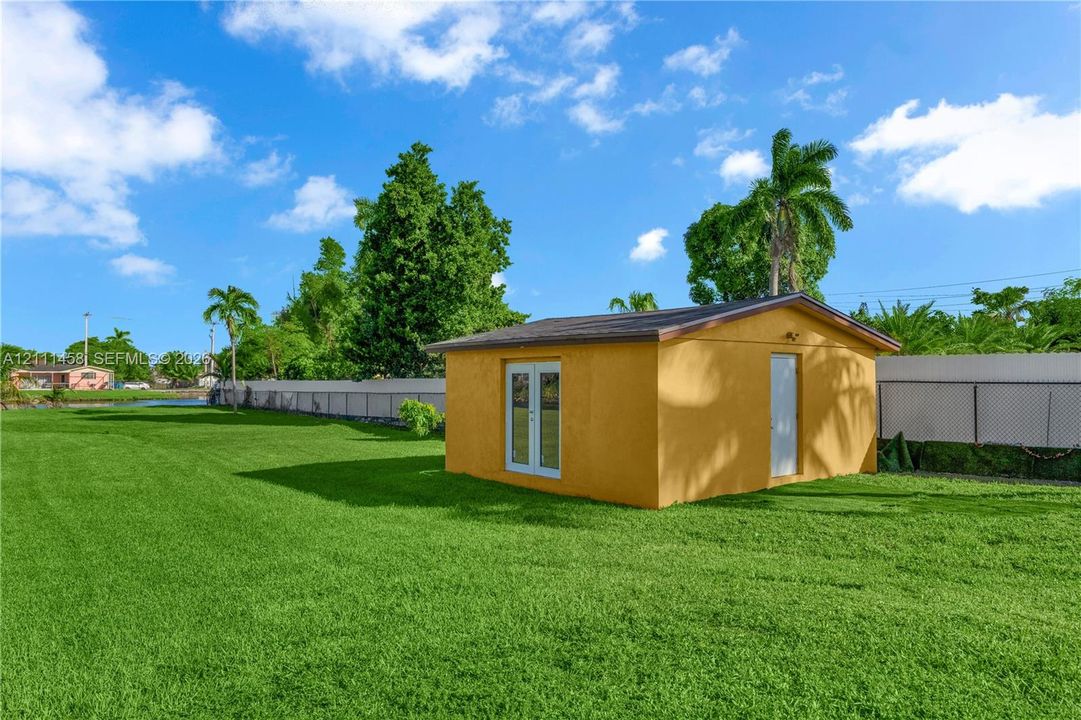 Expansive backyard featuring a manicured lawn, a detached outbuilding, French doors, and perimeter fencing