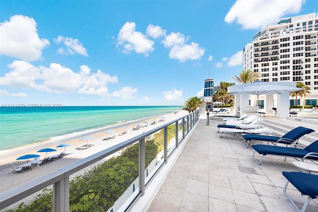 Expansive stone-paved terrace featuring a glass panel railing and direct oceanfront access