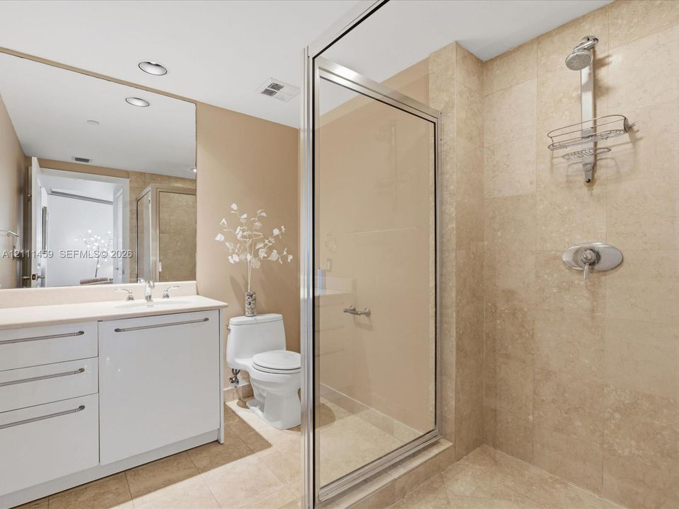 Bathroom featuring a walk-in shower with stone-tile surround, polished chrome fixtures, white vanity with integrated countertop and sink, and a large wall-mounted mirror