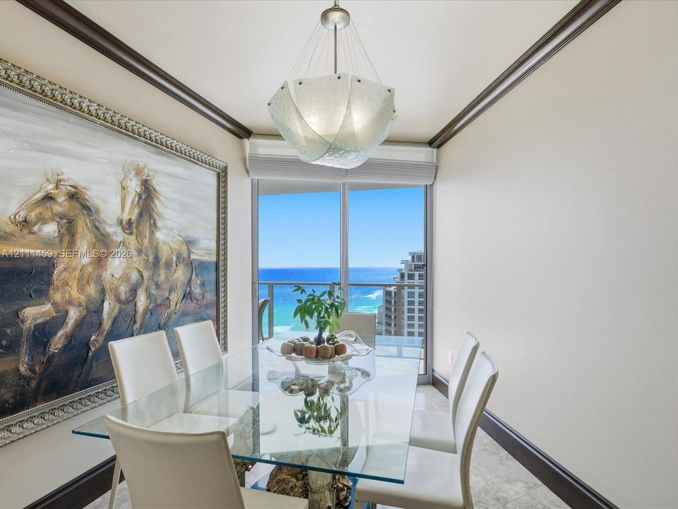 Dining space featuring dark crown molding, stone-finish flooring, a textured glass pendant light, and floor-to-ceiling glass doors opening to a balcony with an ocean backdrop