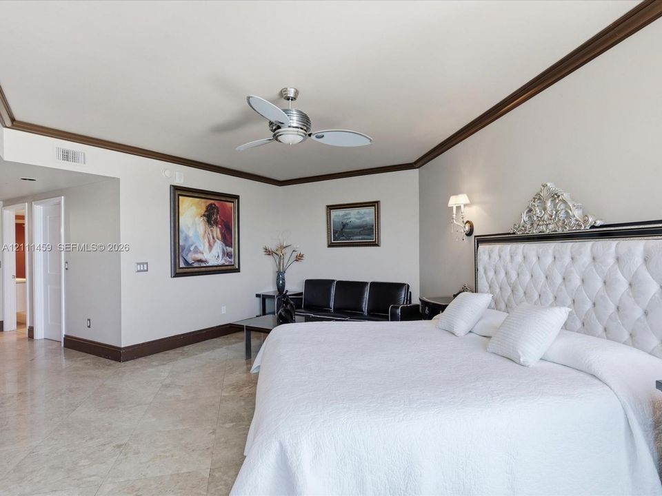 Large room featuring stone flooring, crown molding, wall-mounted light fixtures, and a ceiling fan with integrated lighting