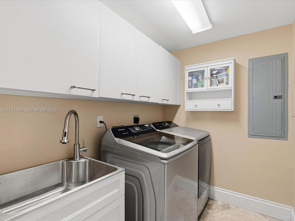 Laundry area featuring white shaker-style wall cabinets, a stainless steel utility sink with a high-arch pull-down faucet, and a wall-mounted glass-front cabinet