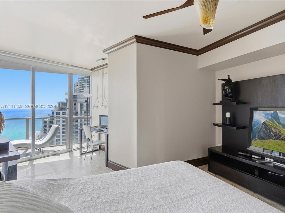 Floor-to-ceiling glass panel windows, built-in media console with tiered shelving, ceiling fan, crown molding, and polished stone flooring