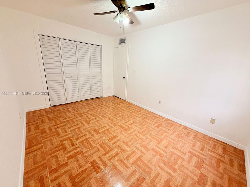Parquet wood-finish flooring, white louvered bifold closet doors, and ceiling-mounted light fixture with a central fan