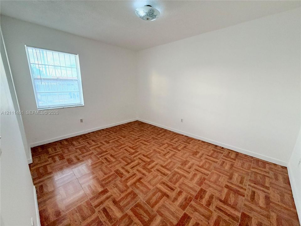 Parquet wood-finish flooring, neutral walls, single-pane window, and flush-mount ceiling fixture