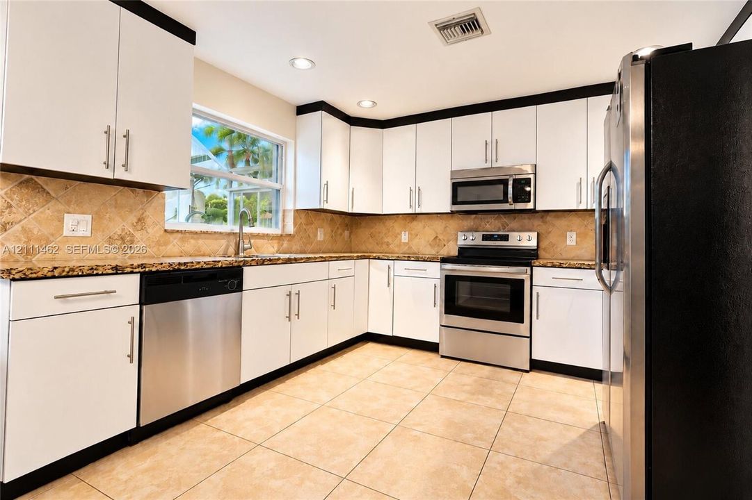 Kitchen featuring white cabinetry with dark crown molding, stone-finish countertops, tile backsplash, stainless steel appliances, and large-format floor tiling