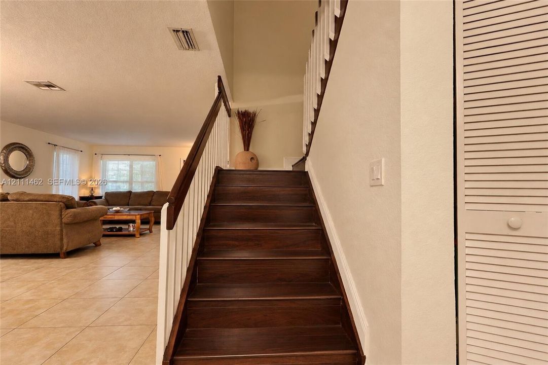 Staircase featuring dark wood-finish treads, white balusters, and a dark wood handrail, paired with neutral floor tiling and louvered closet doors