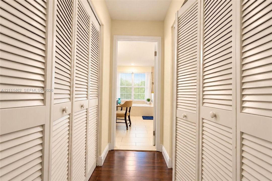 Hallway featuring full-height floor-to-ceiling louvered closet doors, wood-finish flooring, and a multi-pane window